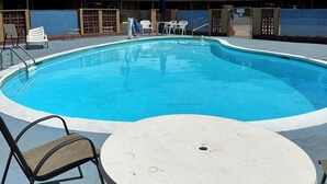 Piscina com espreguiçadeiras e uma mesa, cercada por uma grade e um edifício com a placa 'Budget Motels'.