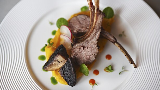 Une assiette contenant une côte d’agneau, des champignons, des radis et des légumes verts.