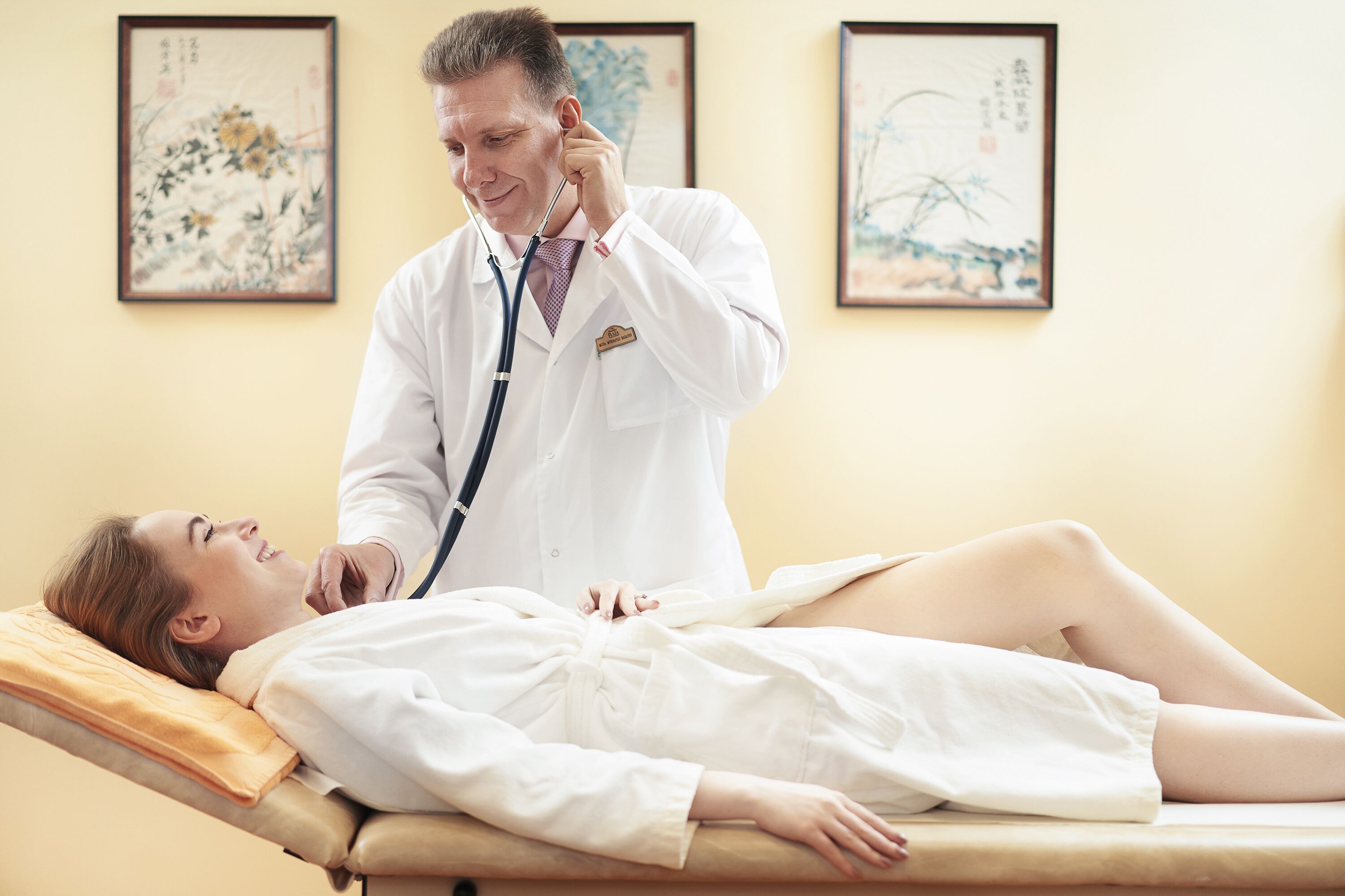 Un profesional médico examina a un paciente en un entorno clínico con obras de arte tradicionales en las paredes.