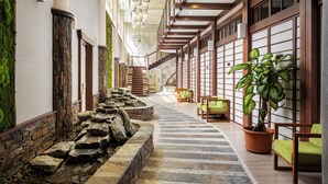 A spacious corridor with a stone water feature, wooden benches, and potted plants.