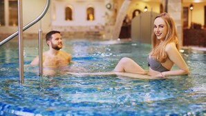 Une piscine à l’eau claire, une échelle en métal et une architecture en pierre en arrière-plan.