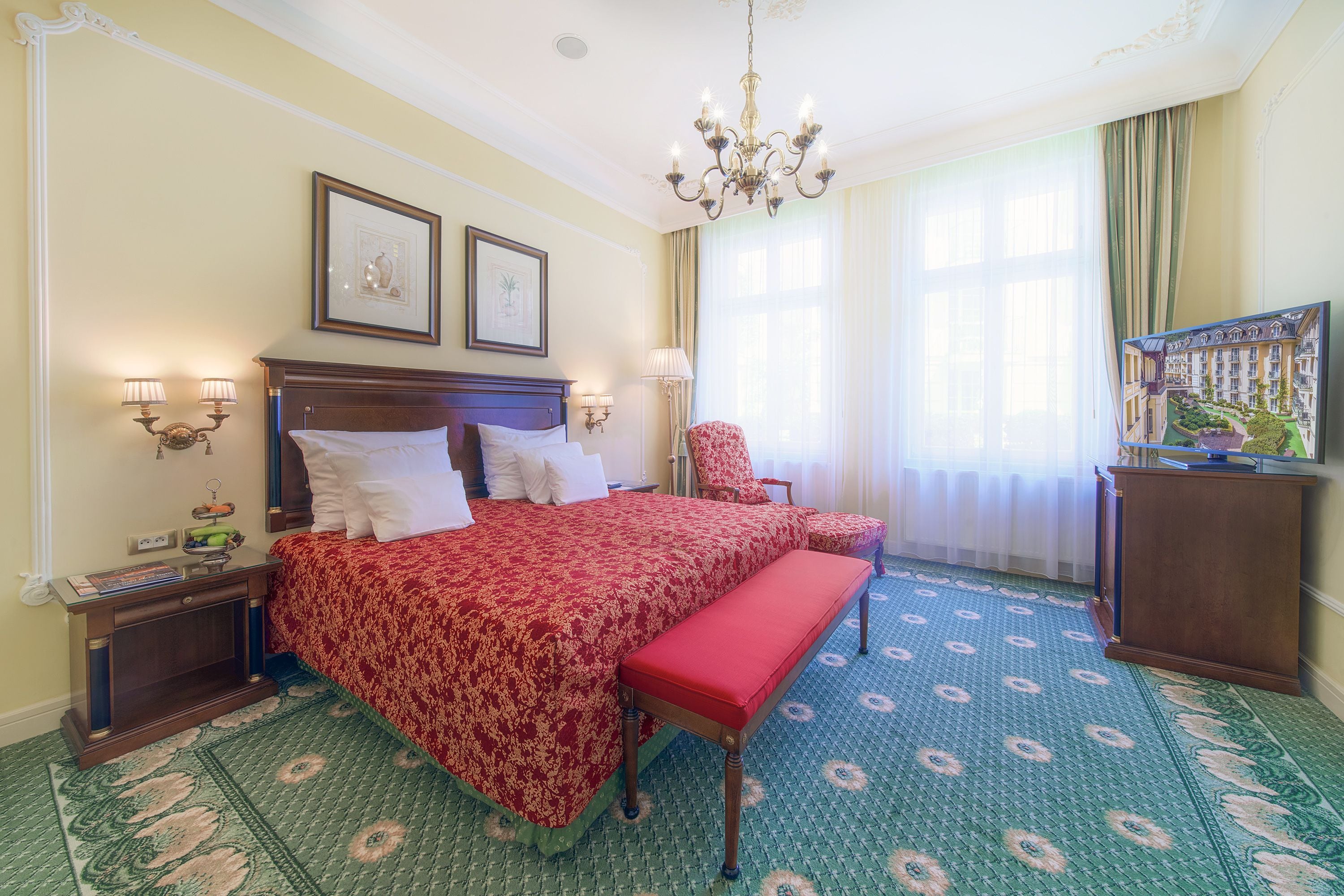 A hotel room with a large bed, a bench, a chair, a desk, and a painting on the wall.