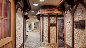 A stone-walled corridor with wooden beams and a tiled floor, leading to a pool area.