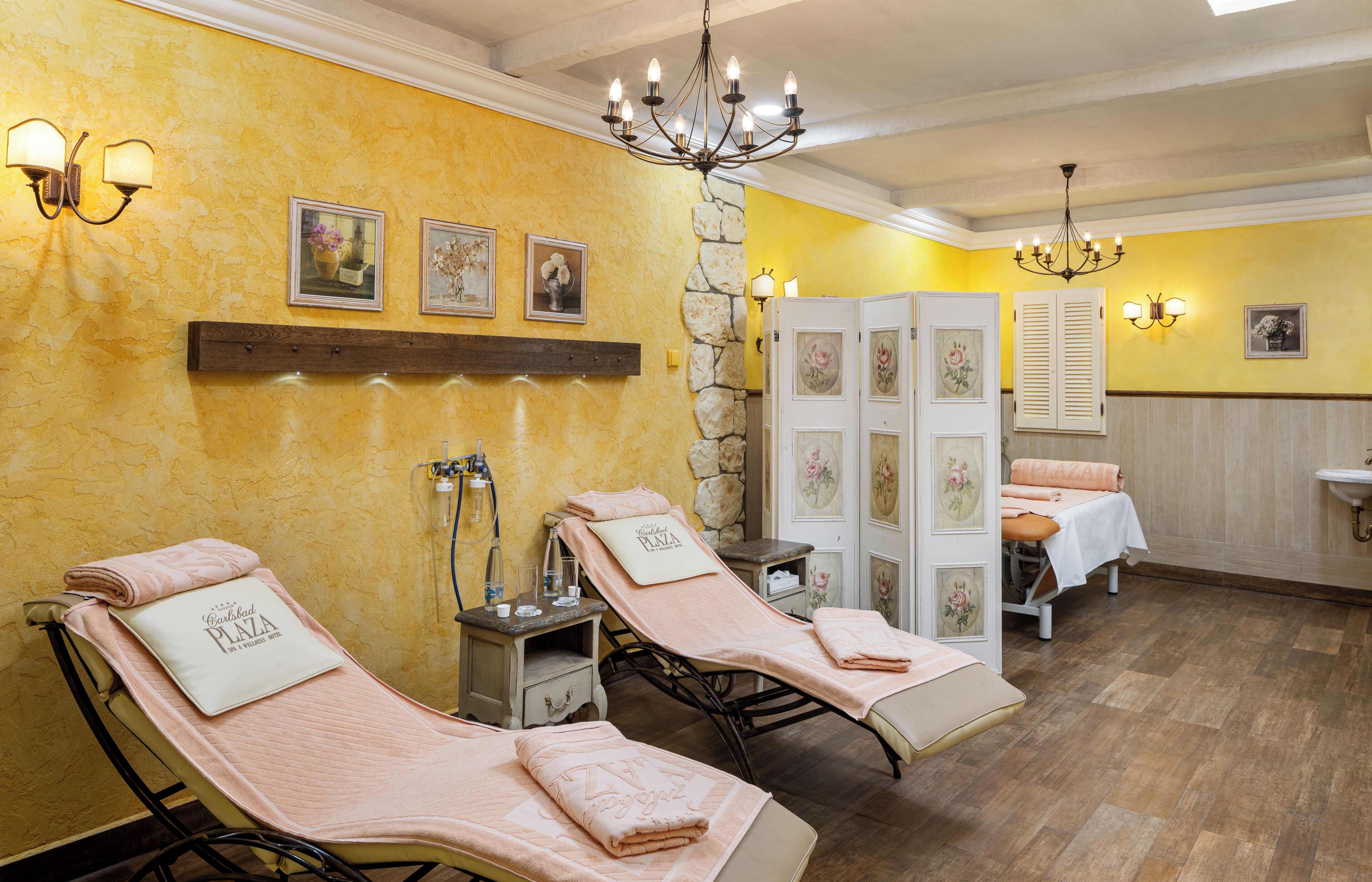 Sala de spa com duas mesas de massagem, parede de pedra e prateleira de madeira com quadros.