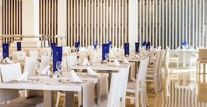 A restaurant with long tables set for dining, featuring white chairs and blue menus.