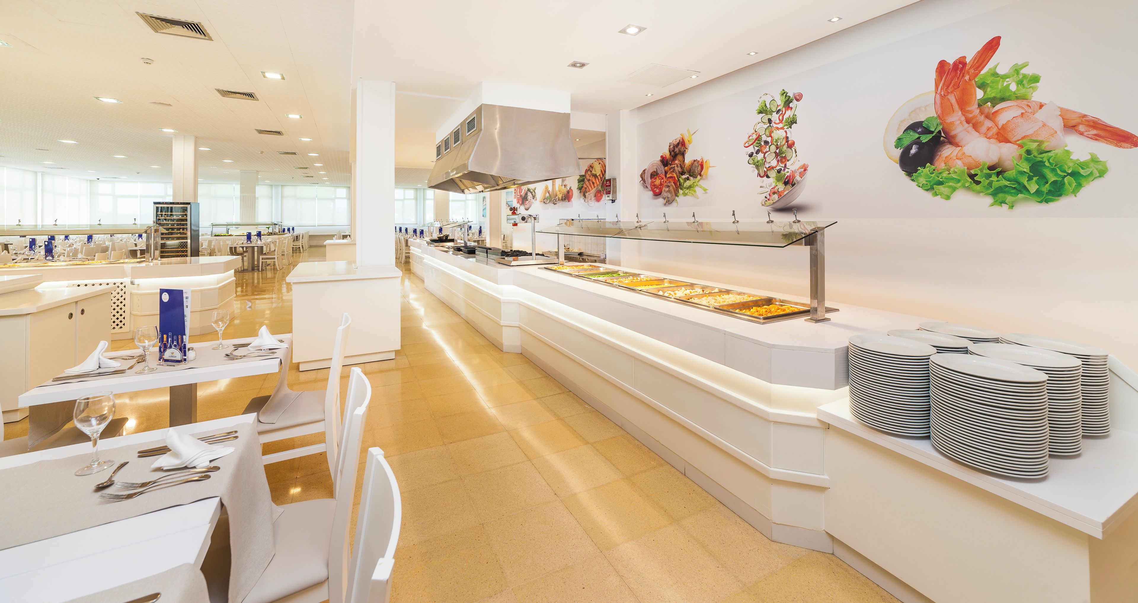 Un'area buffet con diverse postazioni e una parete decorata con illustrazioni a tema gastronomico.