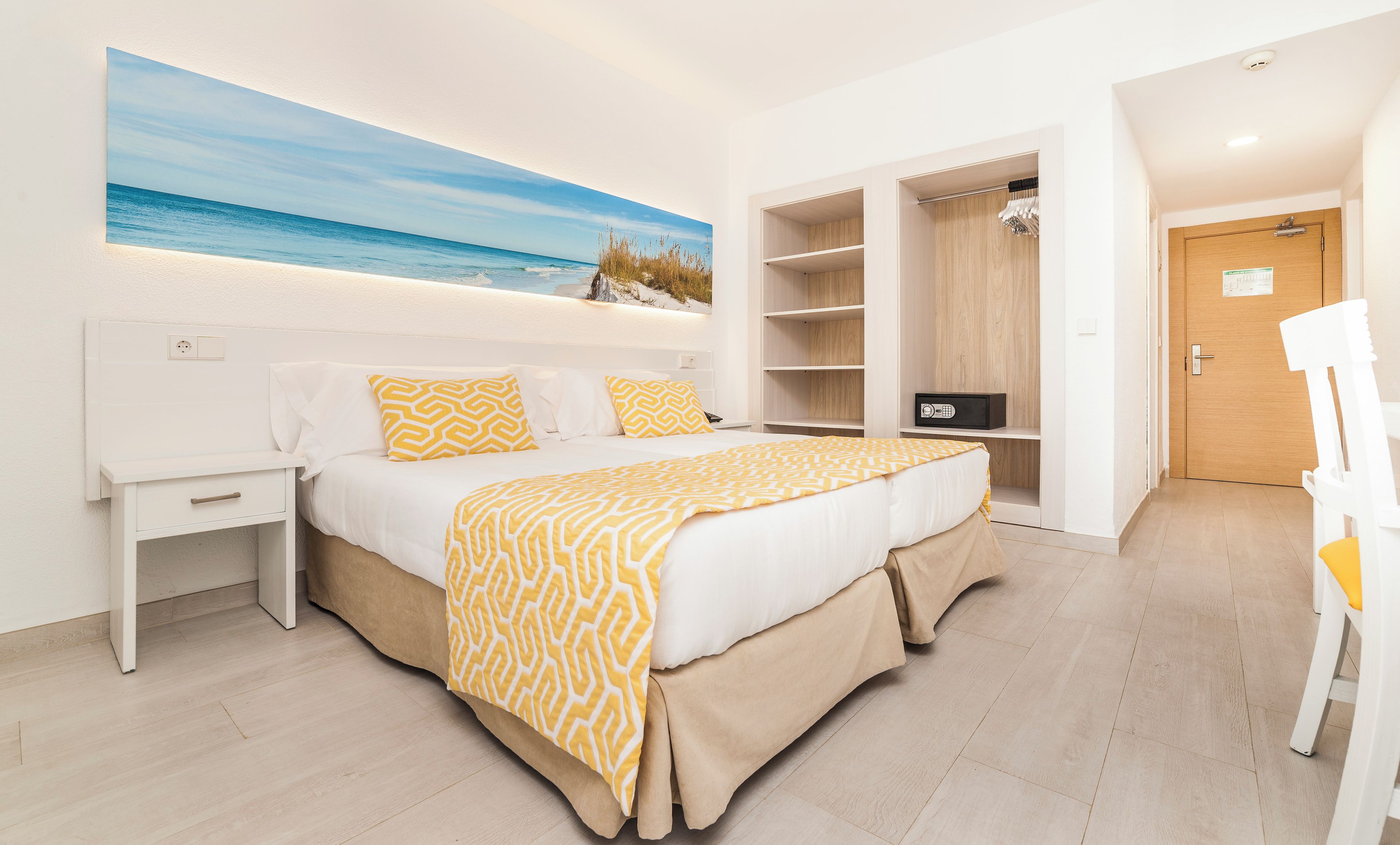 Una camera da letto con un letto, comodini, un armadio e un quadro raffigurante una spiaggia.