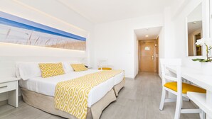 A hotel room with a bed, a desk, and a chair. There is a painting on the wall and a door leading to another room. - Globales Samoa (Manacor)