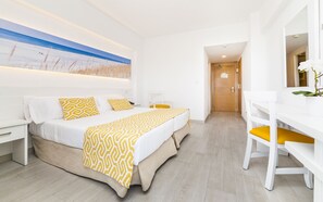 Habitación de hotel con cama, escritorio y silla. Hay un cuadro en la pared y una puerta que da a otra habitación.