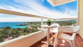 Un balcón con mesa y sillas, una planta en maceta y vistas al mar y al paisaje.