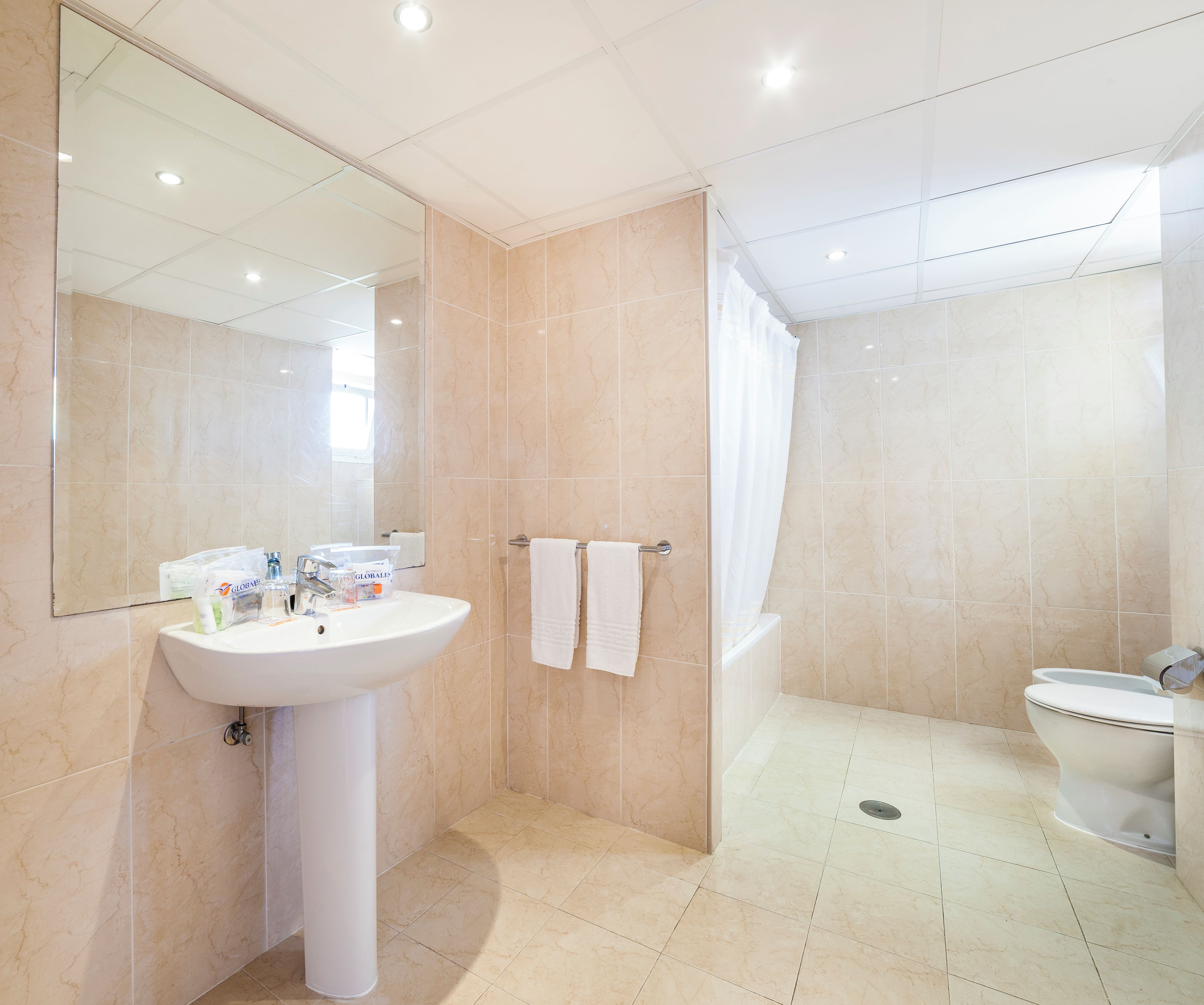Un baño moderno con lavamanos, espejo y dos toallas en un perchero.