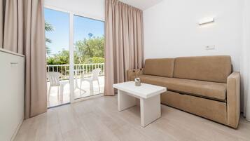 Un soggiorno moderno con un divano beige, un piccolo tavolo bianco e un balcone con sedie bianche.