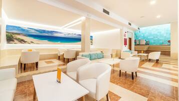 Un moderno vestíbulo de hotel con un mural con vista al mar, muebles blancos y una recepción.