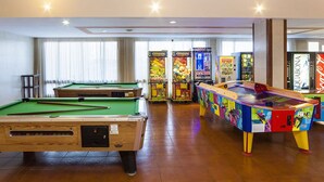 A pool table, arcade machines, and a colorful table tennis table in a room with wooden flooring and large windows. - Globales Samoa (Manacor)