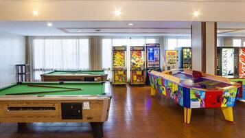 A pool table, arcade machines, and a colorful table tennis table in a room with wooden flooring and large windows.