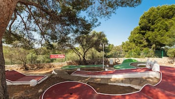 Un campo da miniature golf con un cartello che riporta 'CLUB LOOKÉA', immerso tra alberi e circondato da un muro in pietra.
