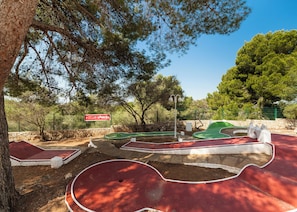 A miniature golf course with a sign for 'CLUB LOOKÉA,' surrounded by trees and a stone wall. - Globales Samoa (Manacor)