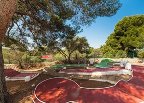 Un campo de mini golf con un cartel que dice 'CLUB LOOKÉA', rodeado de árboles y un muro de piedra.