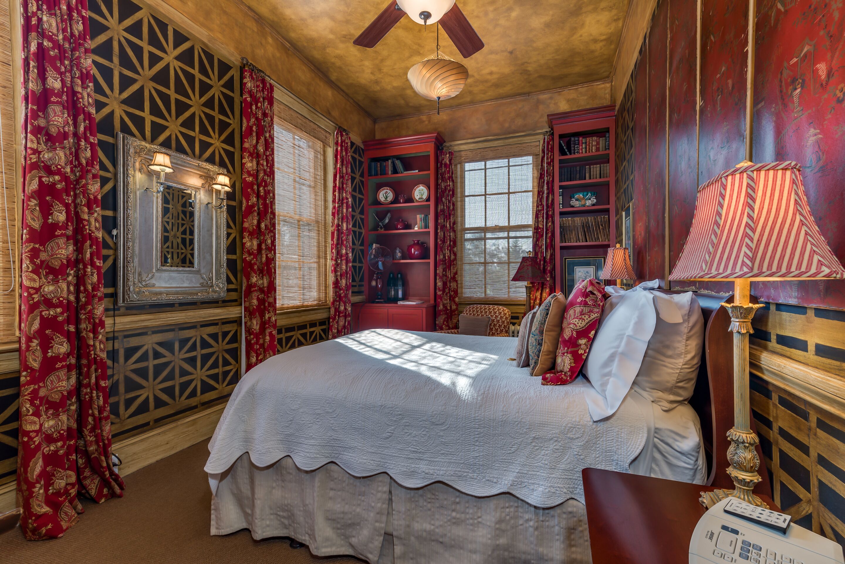 A traditional room with a large bed, bookshelves, and a ceiling fan.