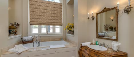 A bathroom with a freestanding bathtub, a vanity with a mirror, and a window with a patterned blind.