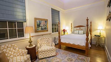 A bedroom with a four-poster bed, a patterned rug, a chair, and a bedside table with a lamp.