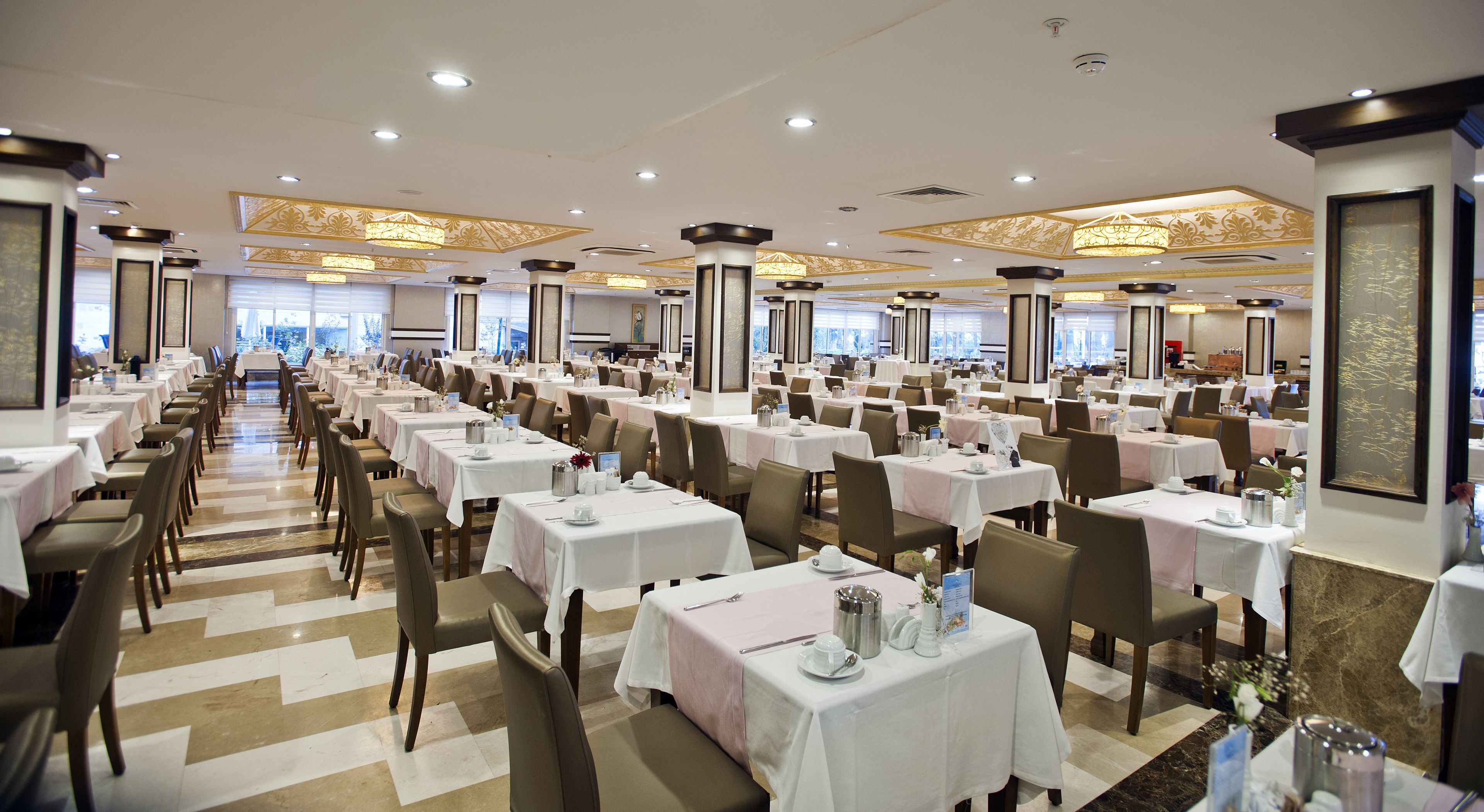 A large banquet hall with multiple tables set for dining, featuring a modern chandelier and a clean, organized layout.