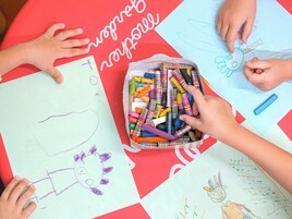 Una mesa con dibujos infantiles y una caja de ceras.