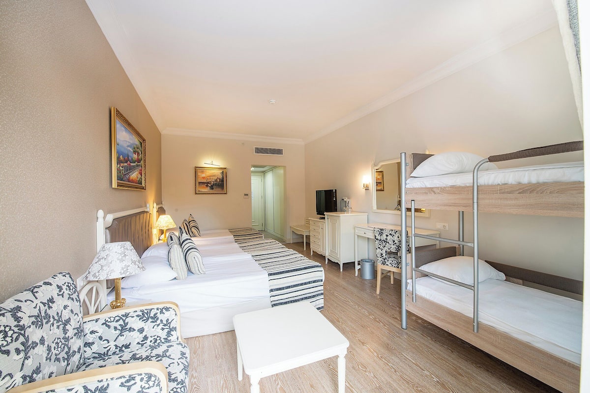 A hotel room with a bunk bed, a sofa, a desk, and a television.