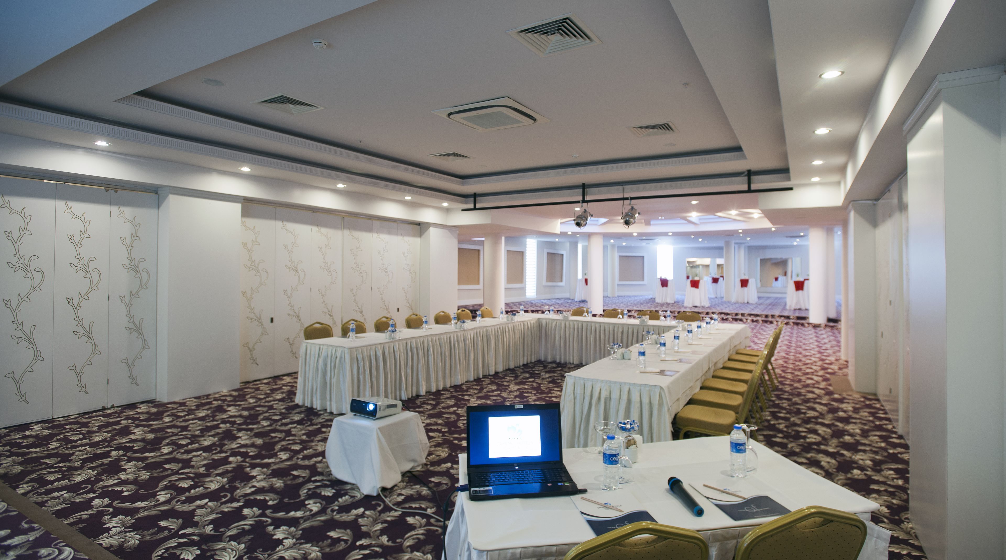 Un salón de conferencias con una larga mesa, sillas y un ordenador portátil sobre la mesa.