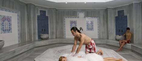 Um quarto de spa com piso de mármore, uma banheira grande e azulejos decorativos azuis nas paredes.