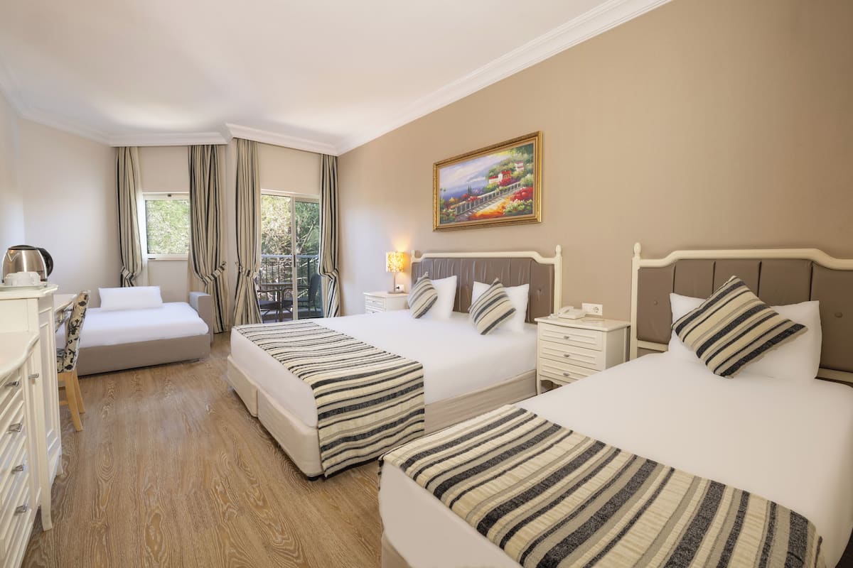A hotel room with two beds, a desk, a chair, a nightstand, a lamp, and a painting on the wall.