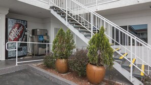 A building with a white exterior, a staircase with white railings, and two large potted plants in the foreground. - Motel 6 Norwalk, CA (Norwalk)