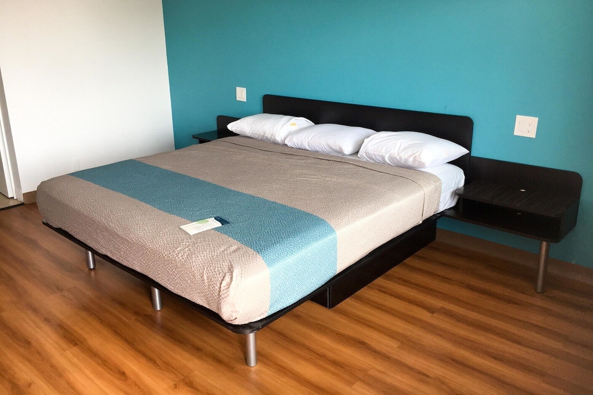 A neatly made bed with a blue and beige bedspread, a black headboard, and a wooden floor.