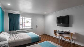 A hotel room with two beds, a TV, a small table with chairs, and a window with curtains.