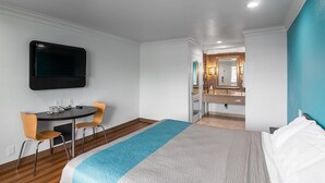 A hotel room with a bed, a desk with a chair, a TV mounted on the wall, and a bathroom with a mirror and sink. - Motel 6 Norwalk, CA (Norwalk)