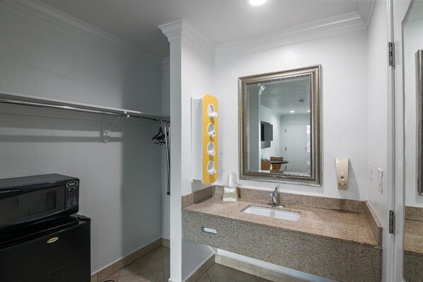 A bathroom with a granite countertop, a sink, a mirror, and a shower area.