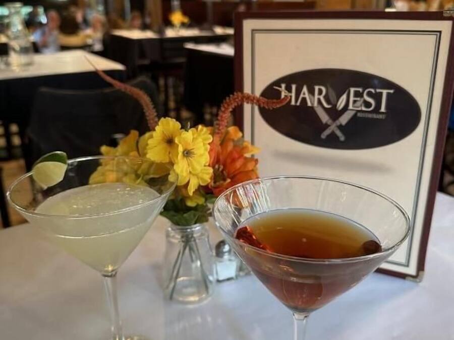 Un interior de restaurante con un cartel enmarcado que dice 'HARVEST' y dos copas de martini sobre una mesa.