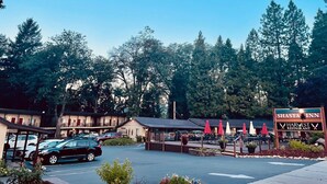 A Shasta Inn with a Harvest Restaurant, surrounded by trees and parked cars.