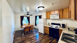 A compact kitchen with wooden cabinets, a microwave, stove, and a dining area with a table and chairs.