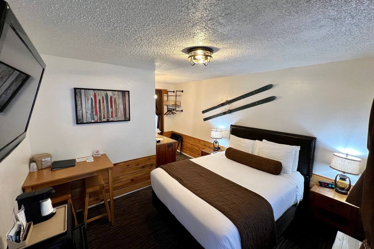 Habitación de hotel con cama, escritorio y silla, un cuadro en la pared y esquíes montados.
