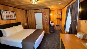 Quarto de cabana de madeira com uma cama grande, uma mesa de madeira, uma TV e esquis pendurados na parede.