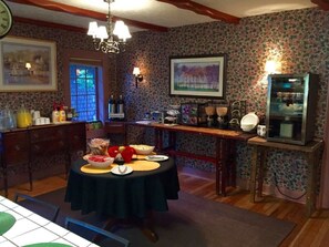 A dining area with a round table set for four, surrounded by floral wallpaper, a chandelier, and a refrigerator.