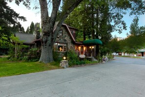 A stone house with a porch and a green awning, surrounded by trees and a clear sky.