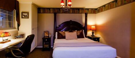 Une chambre d’hôtel avec un lit à baldaquin, un bureau avec une chaise, une lampe de bureau, une table de chevet avec une lampe et un tableau au mur.