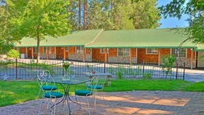 A building with a green roof and stone walls, surrounded by a fenced garden with a paved patio and metal chairs. - Strawberry Valley Inn (Mount Shasta)