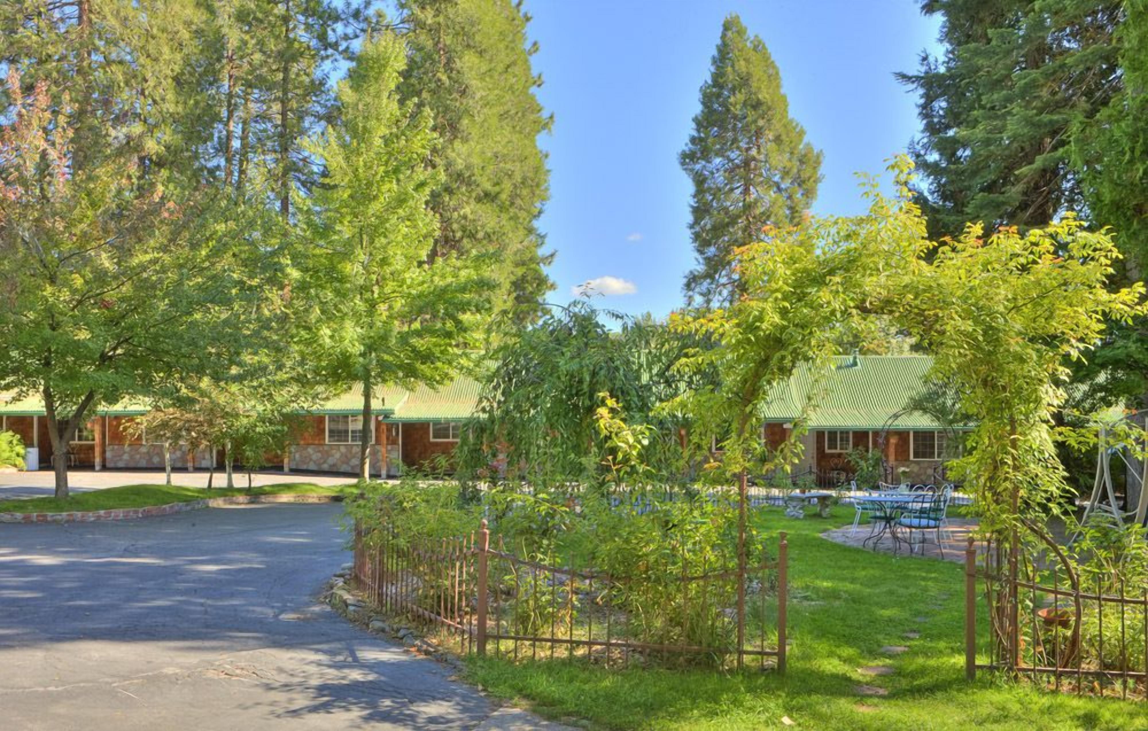 A lodge with a stone exterior, surrounded by tall trees and a fenced outdoor area with tables and chairs.