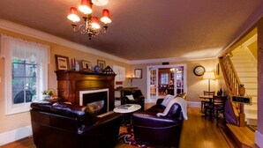 A cozy living room with a fireplace, leather sofas, a chandelier, and a staircase leading to another level. - Strawberry Valley Inn (Mount Shasta)