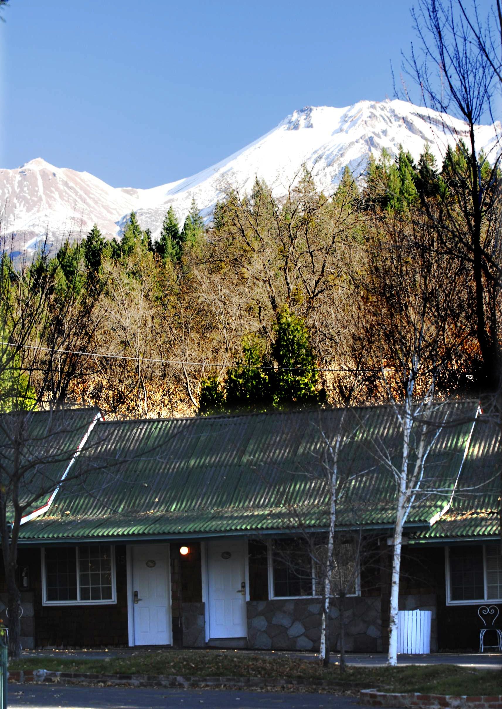 A lodge with a green roof, stone walls, and a view of a snow-capped mountain.