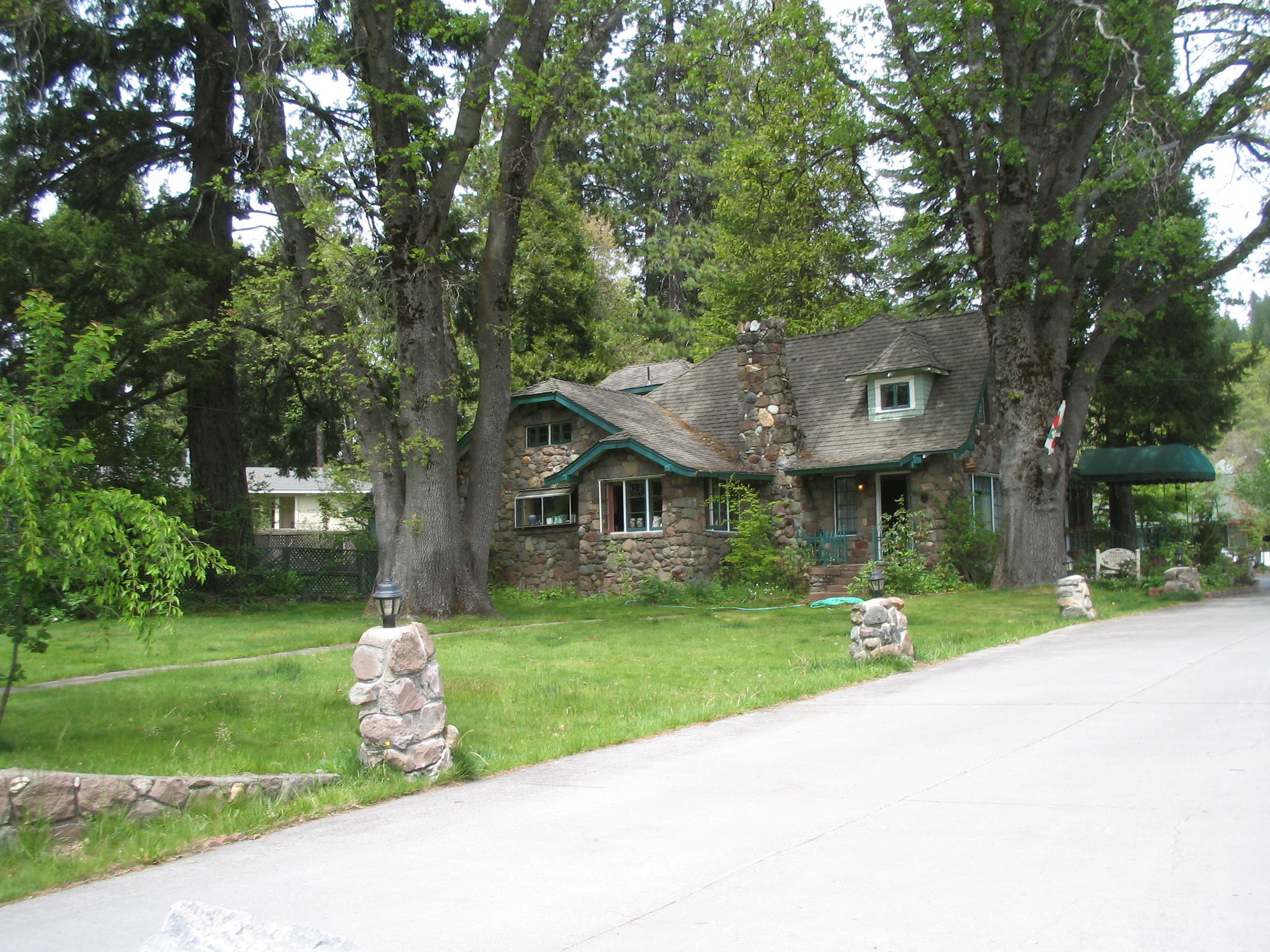 Une maison en pierre avec un toit végétalisé, entourée d’arbres et d’une pelouse bien entretenue.