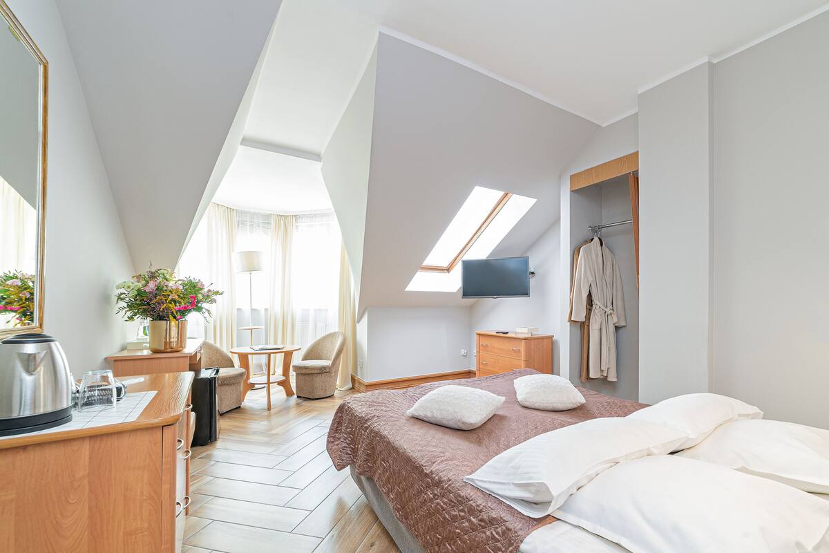 Una habitación de hotel moderna con una cama grande, un escritorio con hervidor, una silla, un televisor y un armario.
